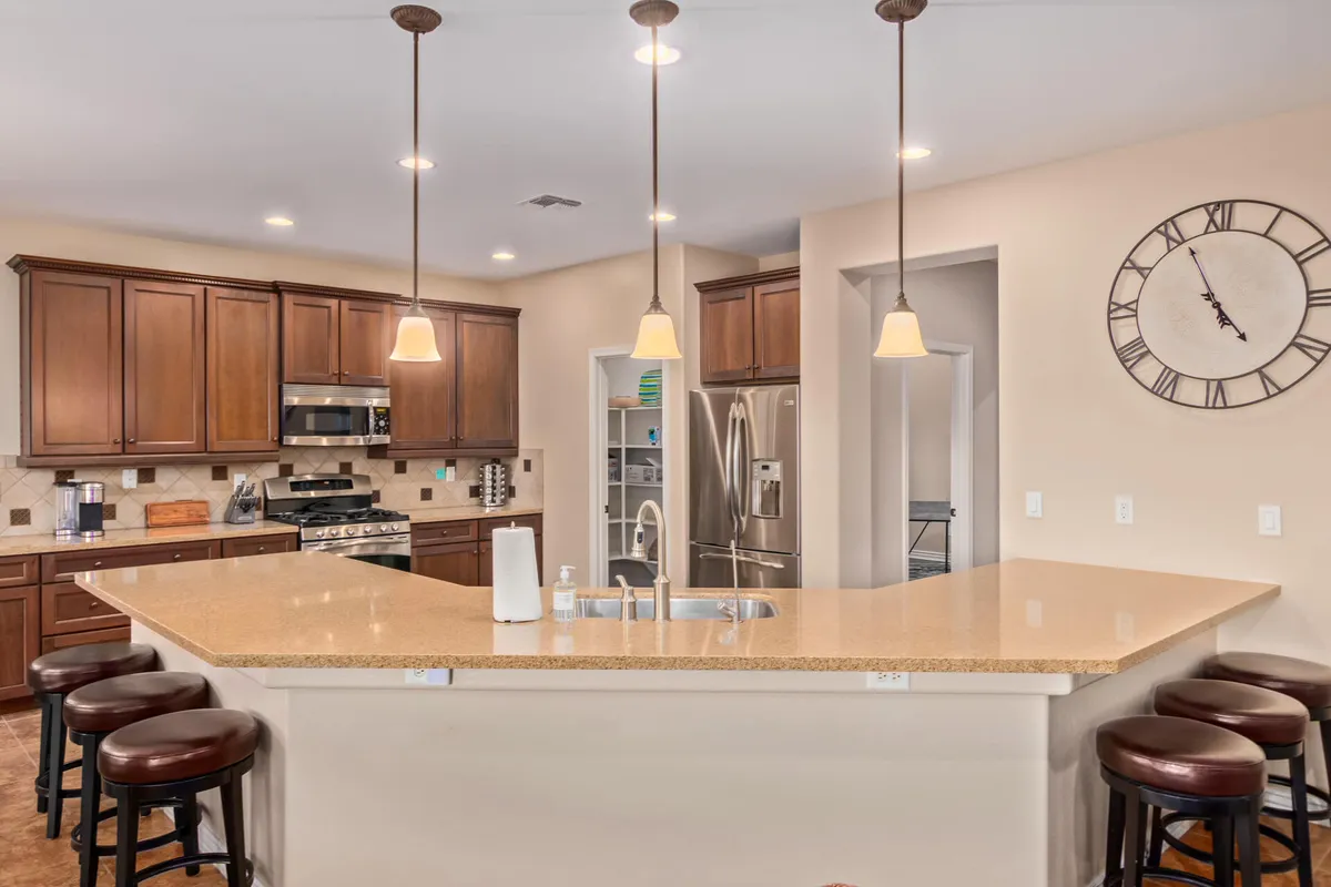 This image showcases a warm and welcoming kitchen with an island countertop, stool seating, kitchen cabinets, modern appliances, and a distinct wall clock. The materials and finishes hint at a fusion of contemporary design with subtle Southwestern influences, while the space looks ready for both daily meal prep and festive gatherings.