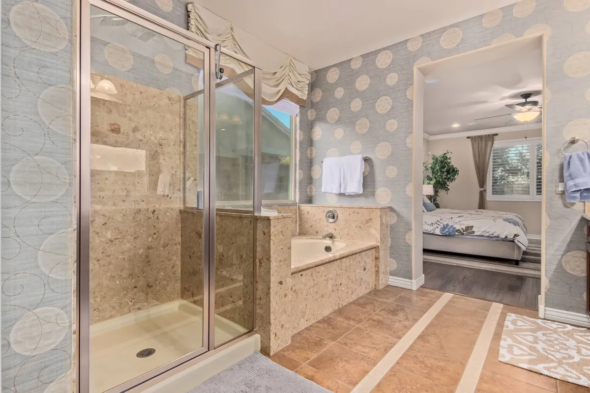 A serene bathroom featuring a shower enclosure, bathtub, decorative wallpaper, and plush towels. The layout and decor evoke calmness and provide an inviting space for self-care routines and relaxation.