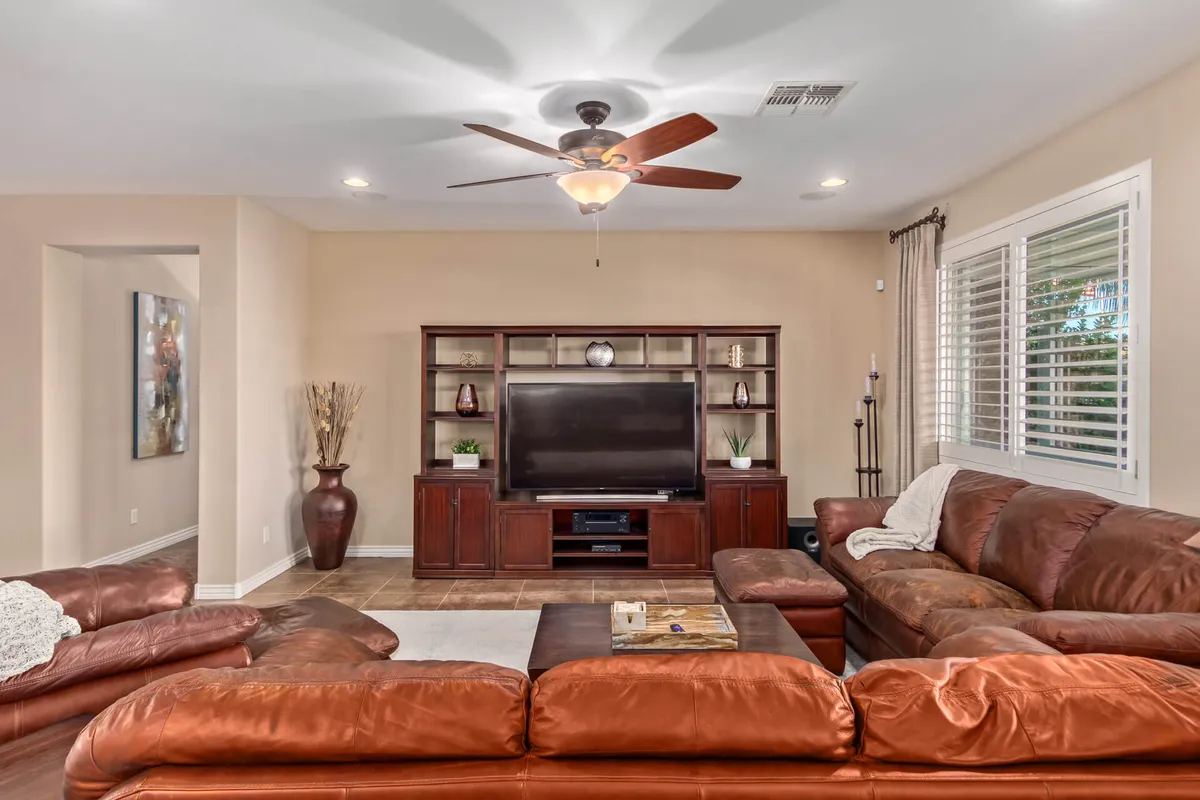 A spacious living room featuring a large brown leather sectional sofa, entertainment unit with a TV, and decorative items on the shelves. The setting is cozy, with soft lighting and an inviting arrangement perfect for gathering with family or friends.