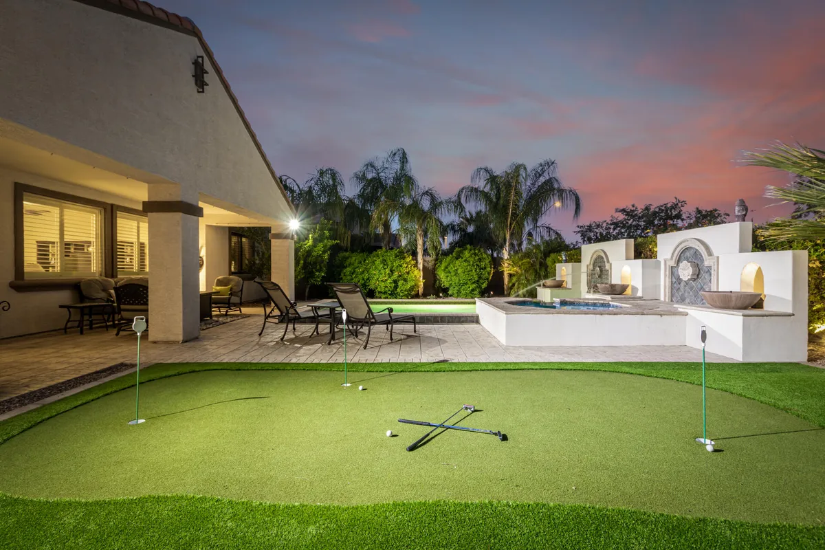An inviting outdoor space with a golf putting green, bubbling hot tub, comfortable seating area, and abundant greenery. The area is designed for sunset golf practice, social gatherings, and relaxing after a day on the course.