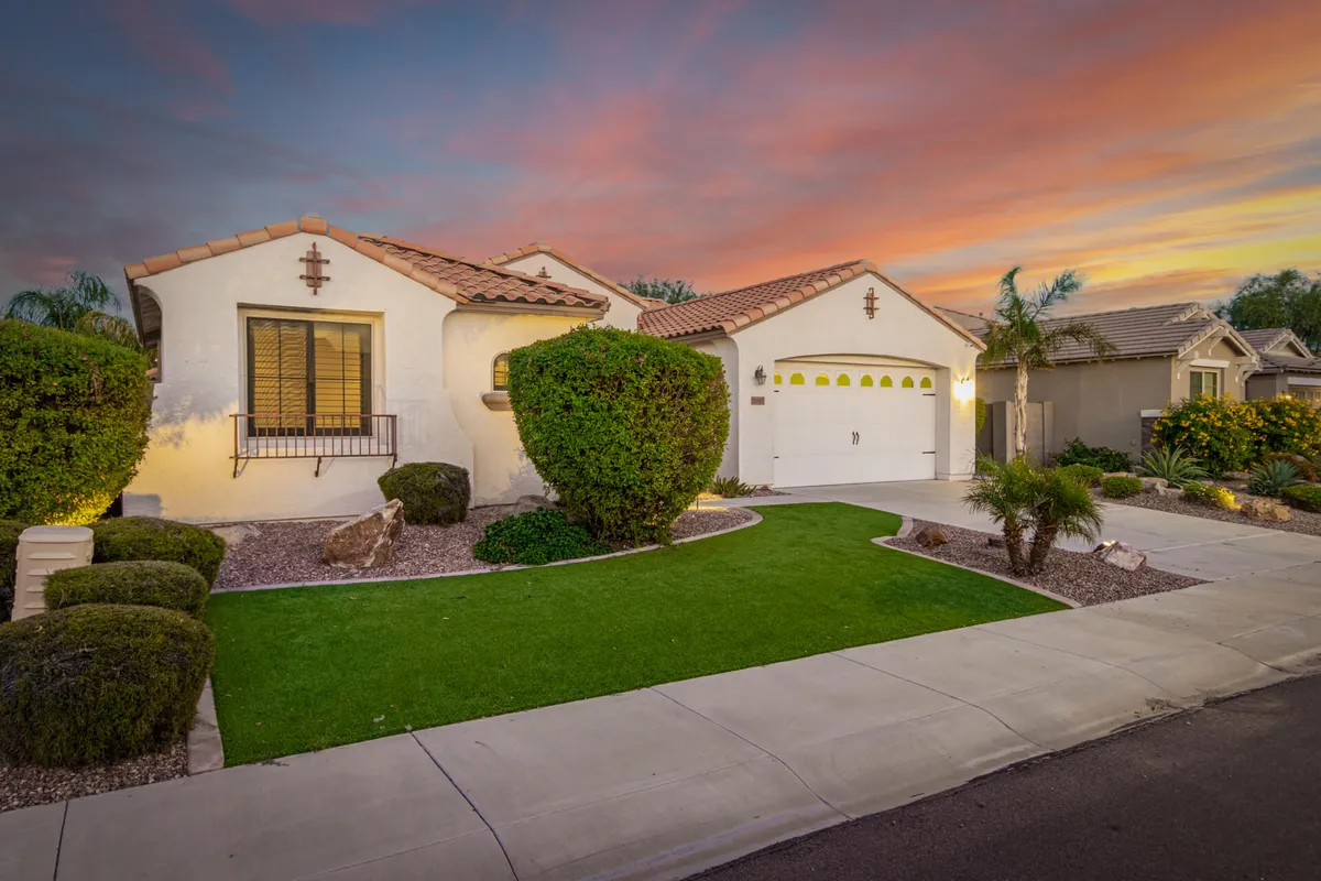 A beautifully maintained front lawn with vibrant shrubs, a spacious porch, and a colorful sunset sky in the background. The scene is peaceful and welcoming, hinting at neighborhood tranquility and the joy of spending time outdoors at home.