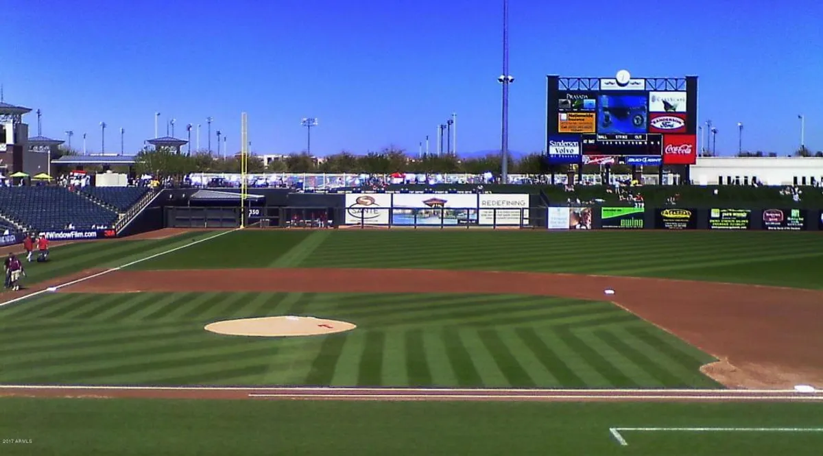 A bustling baseball field with a clearly visible scoreboard and audience seating. Fans are gathered in the stands, creating an energetic atmosphere that highlights the excitement of live sports events typical of Spring Training seasons.