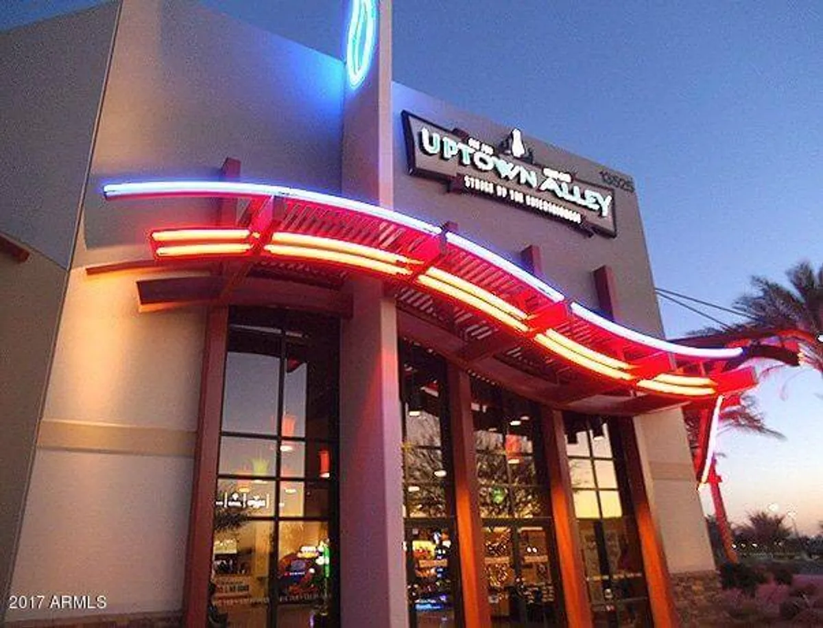 A lively exterior scene featuring neon lights and a prominent entrance sign, evoking the energetic vibe of an entertainment district. Architectural features and illuminated signage hint at nightlife, dining, and fun social gatherings.