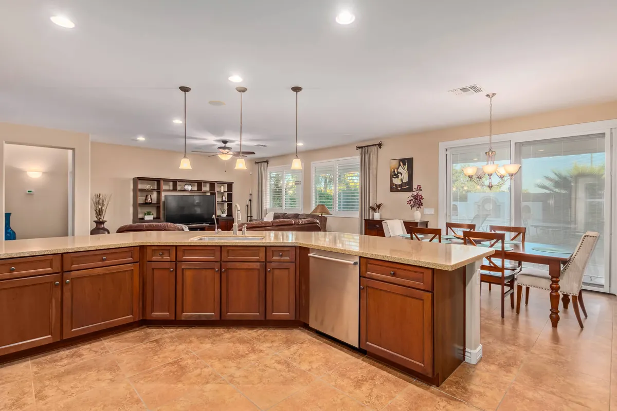 A spacious, open-concept kitchen and living area is depicted, featuring a prominent kitchen island, sleek cabinets, an adjacent dining area, and comfortable living room seating. The setting is bright and open, showcasing materials and décor that evoke Southwestern warmth and hospitality.