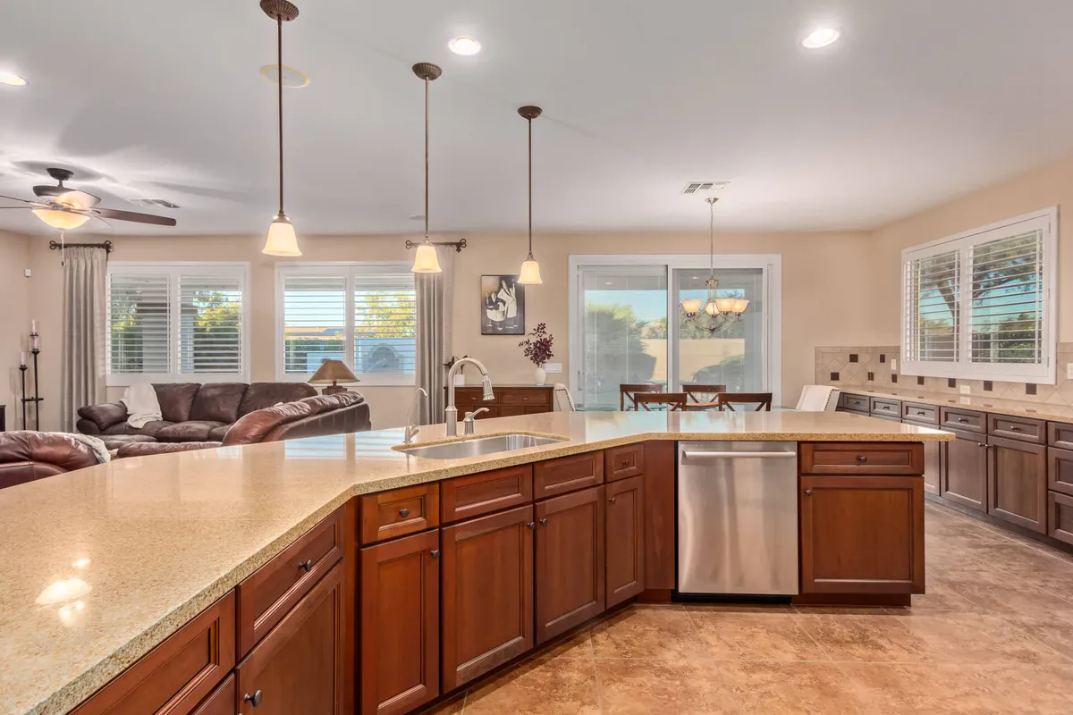 A kitchen scene featuring a granite countertop, prominent kitchen island, recessed lighting, and a dining area surrounded by large windows. The ample natural light and earthy tones evoke the sunlit, nurturing atmosphere described for the breakfast nook.